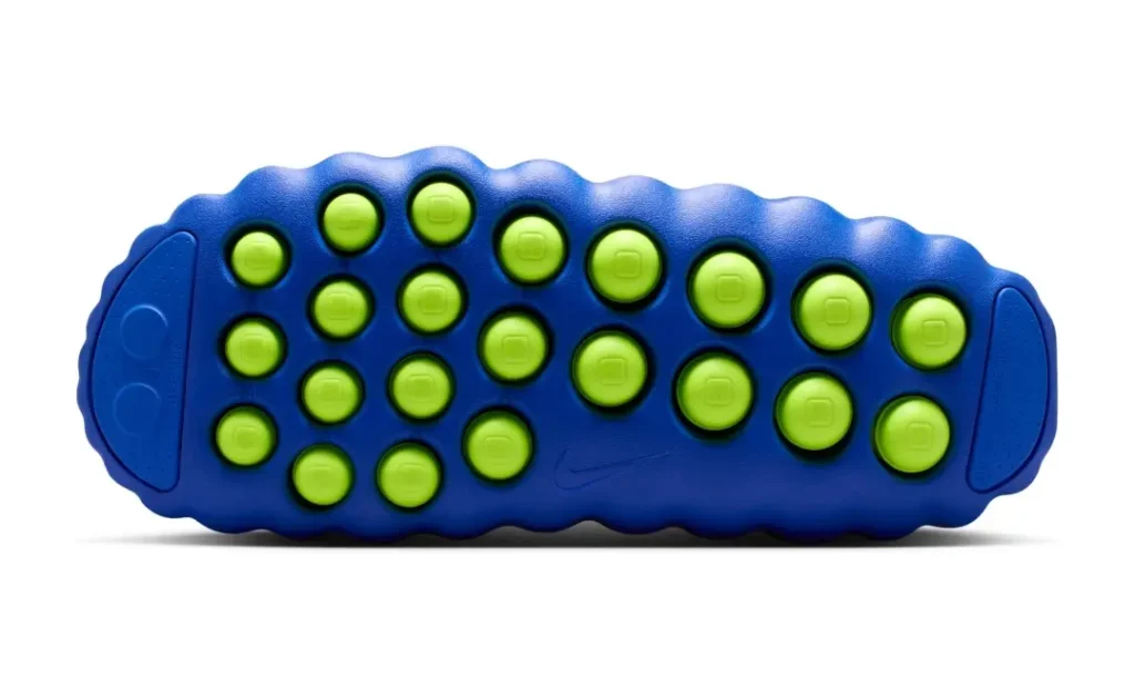 Outsole detail image of the Nike Mind 001 Flyknit QS “Hyper Royal/Volt,” highlighting its signature sensory-driven traction system. The vivid Hyper Royal blue sole features 22 circular Volt foam nodes arranged across the full length of the foot, creating a piston-like, pressure-responsive layout inspired by neuroscience and plantar stimulation. Sculpted wave edges frame the outsole, while subtle Nike branding appears at the center for a clean, futuristic finish