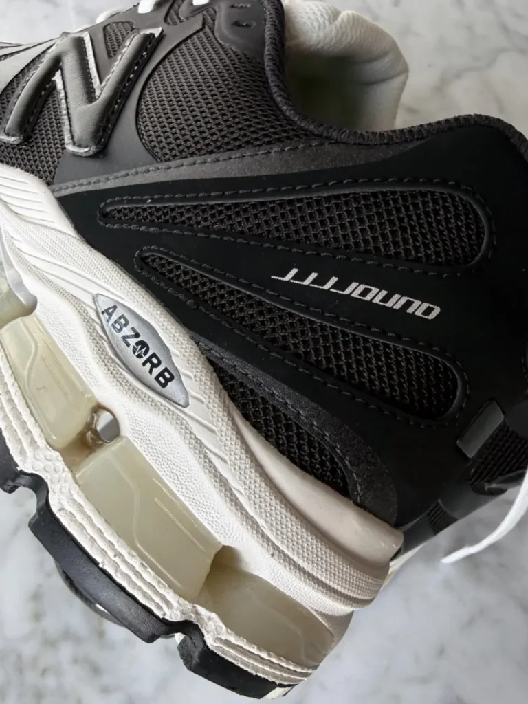 Close-up detail of a black mesh New Balance-style running shoe featuring layered synthetic overlays, reflective “N” branding, cream ABZORB cushioning pods, and a sculpted off-white midsole with visible aged translucent support elements