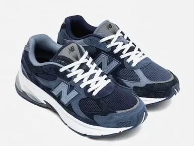 Angled product image of the New Balance x BEAMS 2010 “Navy” shoe showcasing layered navy suede overlays, breathable mesh underlays, oversized white midsoles, and crisp white laces against a muted grey studio background