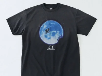 Black graphic T-shirt featuring the iconic moon silhouette scene from E.T., with the bicycle and alien crossing the glowing blue moon and subtle film logo beneath