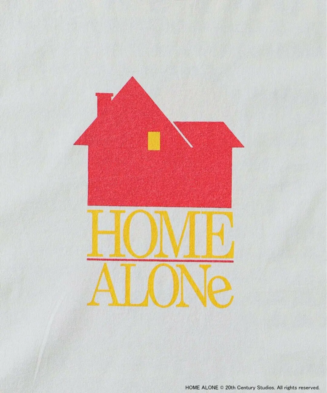 Close-up of off-white Home Alone graphic T-shirt featuring a bold red house icon above vintage yellow Home Alone typography in a clean retro film poster style