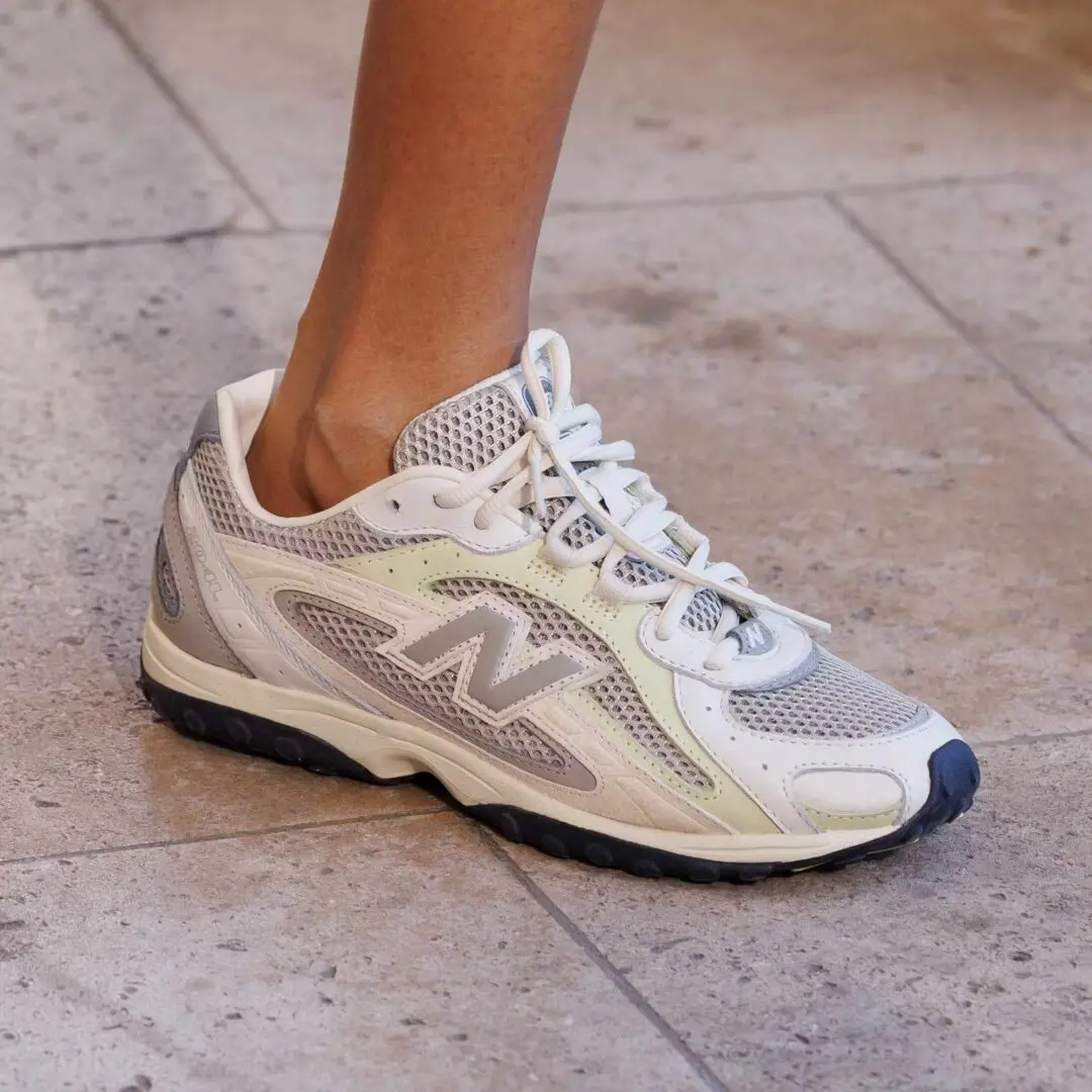 A silver-and-white mesh runner with layered metallic overlays, pale cream accents, and dark contrast outsoles merges archival performance design with contemporary lifestyle styling. The streamlined silhouette reflects the continued dominance of lightweight retro-running sneakers within modern fashion and runway culture
