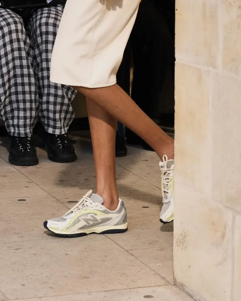 A silver-and-white retro runner pairs breathable mesh paneling with layered metallic overlays and soft cream midsoles, reflecting the continued rise of streamlined performance-inspired sneakers within modern runway styling