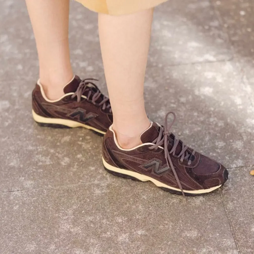 A deep brown retro runner with layered suede panels, breathable mesh inserts, and cream-toned midsoles channels a softened archival running aesthetic through a more fashion-oriented lens. The streamlined silhouette continues the broader move toward understated technical sneakers with vintage-inspired detailing and everyday versatility