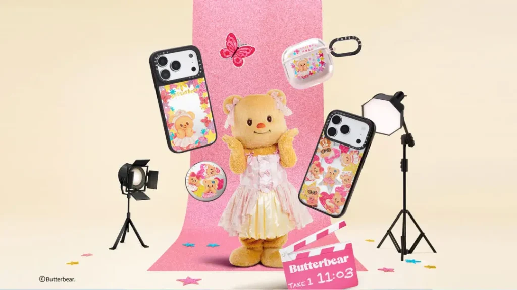 Promotional image of Butterbear posing in a pastel dress on a studio-style set surrounded by CASETiFY tech accessories, including floral phone cases, AirPods cases, and collectible charms against a pink backdrop with photography lighting props