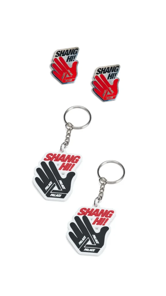 Palace Shanghai collectible accessories featuring enamel pins and acrylic keychains shaped like the brand’s signature hand-and-Tri-Ferg graphic. The design combines bold “SHANG HI!” typography with red, black, and white color blocking, extending the playful visual identity of the Shanghai flagship collection into everyday carry items