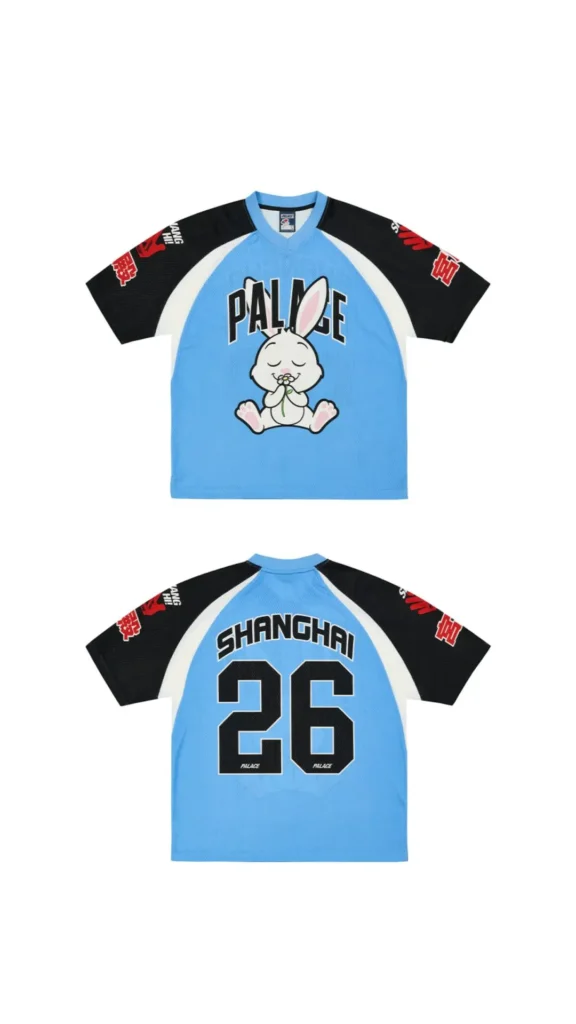 Front and back views of a Palace Shanghai jersey in powder blue with black raglan sleeves, featuring oversized Palace lettering and a cartoon rabbit graphic on the front. The reverse displays “SHANGHAI” above the number “26,” while red sleeve graphics and sport-inspired detailing give the piece a playful, localized take on vintage team uniforms for the Shanghai flagship collection