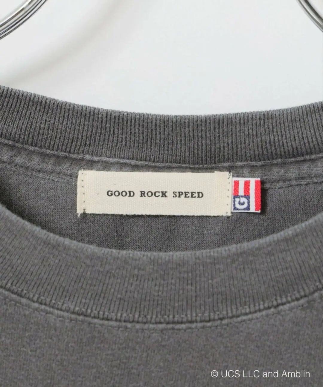 Close-up of the GOOD ROCK SPEED woven neck label stitched inside a washed grey cloth T-shirt with ribbed collar detai
