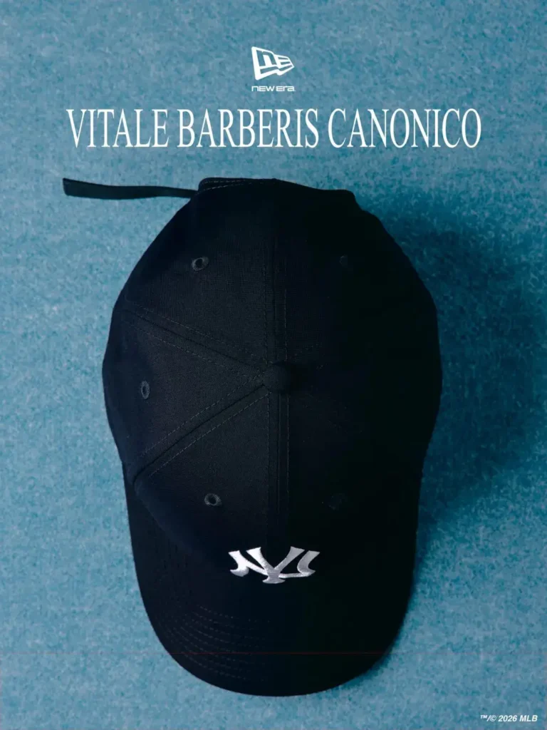 Top-down view of a minimalist black New Era 9FORTY Yankees cap crafted from premium Vitale Barberis Canonico wool, featuring subtle tonal stitching and a clean panel structure without pinstripes. Positioned beneath oversized “Vitale Barberis Canonico” branding on a textured icy-blue backdrop, the design highlights refined construction, understated luxury, and modern tailored sportswear sensible