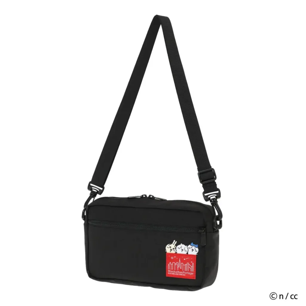 A minimalist studio image of a compact Manhattan Portage x Chiikawa shoulder bag finished in matte black nylon with an adjustable crossbody strap and multiple zip compartments. The streamlined rectangular silhouette reflects Manhattan Portage’s everyday urban utility design language, while the collaboration’s playful identity appears through embroidered Chiikawa characters emerging above the iconic red skyline label on the front panel. The soft gray backdrop emphasizes the balance between functional citywear aesthetics and kawaii-inspired character detailing