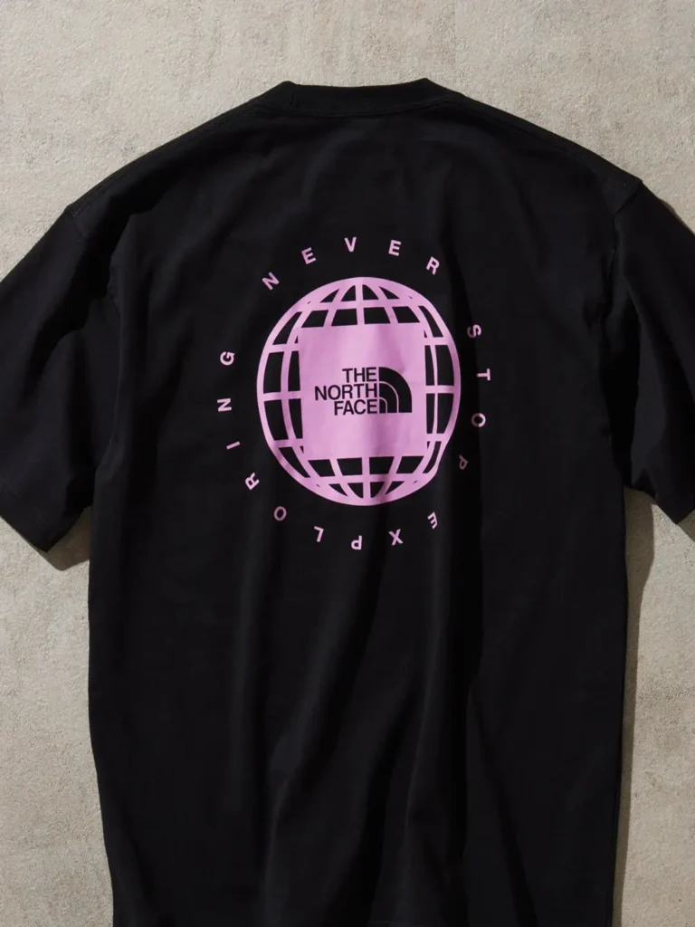 Black The North Face T-shirt with a large pink globe graphic on the back and circular “Never Stop Exploring” typography surrounding the centered logo