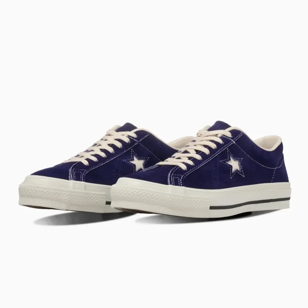 Angled product shot of the Converse TimeLine ONE STAR J VTG “Purple,” showing a pair of low-top sneakers in rich archival purple suede with crisp white contrast stitching, vintage-scale One Star logos, and off-white laces. The clean white vulcanized sole and low-profile shape emphasize the model’s 1974 basketball heritage with refined Made-in-Japan execution