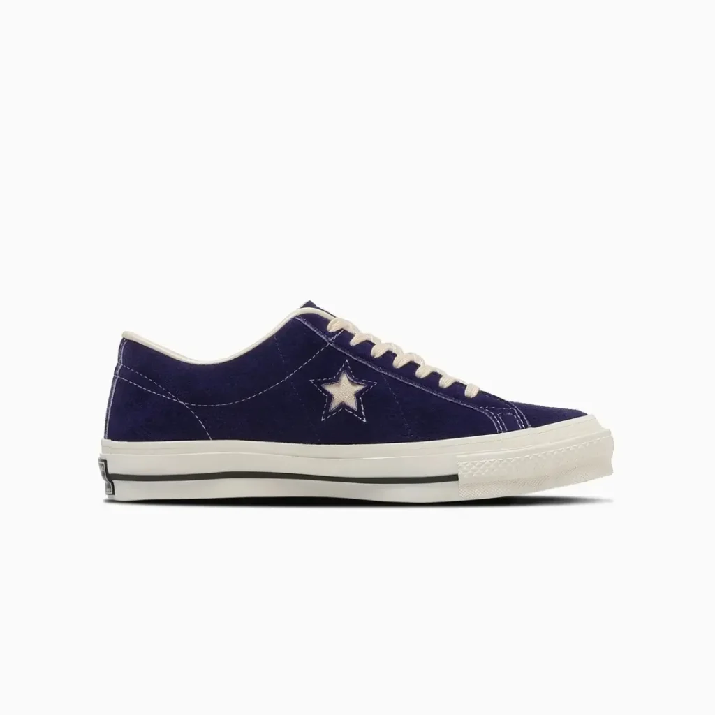 Lateral profile product image of the Converse TimeLine ONE STAR J VTG “Purple,” highlighting the low-cut silhouette in rich vintage-inspired purple suede with tonal paneling, white contrast stitching, and the signature cut-out One Star logo. Off-white laces and a classic white vulcanized sole with black foxing stripe complete the faithful Made-in-Japan recreation of the original 1974 basketball design