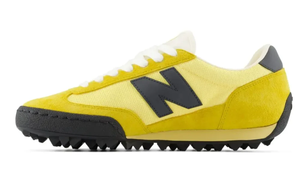 Side profile view of the New Balance Gator Run U GTR 9SR “Apollo Gold/Black” featuring rich yellow suede overlays, pale yellow mesh construction, oversized black New Balance branding, white laces, and a rugged pyramid-style outsole that references the silhouette’s original 1982 turf trainer heritage