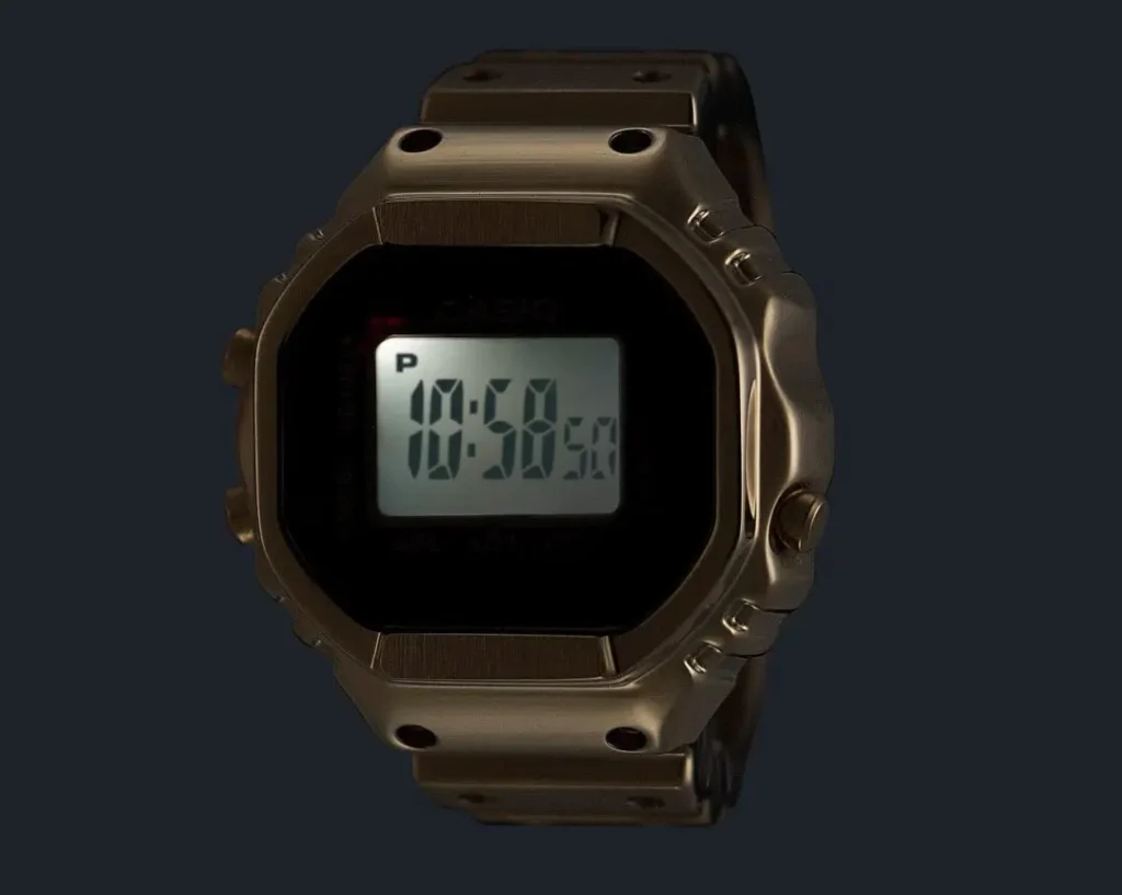Close-up of the gold Casio Ring Watch digital display illuminated against a dark background, showcasing the retro-inspired miniature timekeeping interface and metallic finish