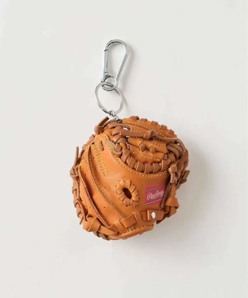 Studio product image of a miniature Rawlings catcher’s mitt keychain in tan leather with intricate hand-laced detailing, contrast stitching, silver clasp hardware, and heritage logo accents displayed against a minimalist white backdrop