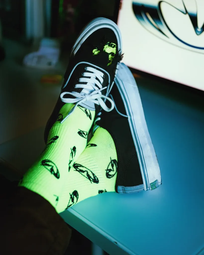 On-foot view of the Vans x GUCCIMAZE PREMIUM AUTHENTIC paired with neon green patterned socks, revealing the sneaker’s wear-away upper and reflective trim detail