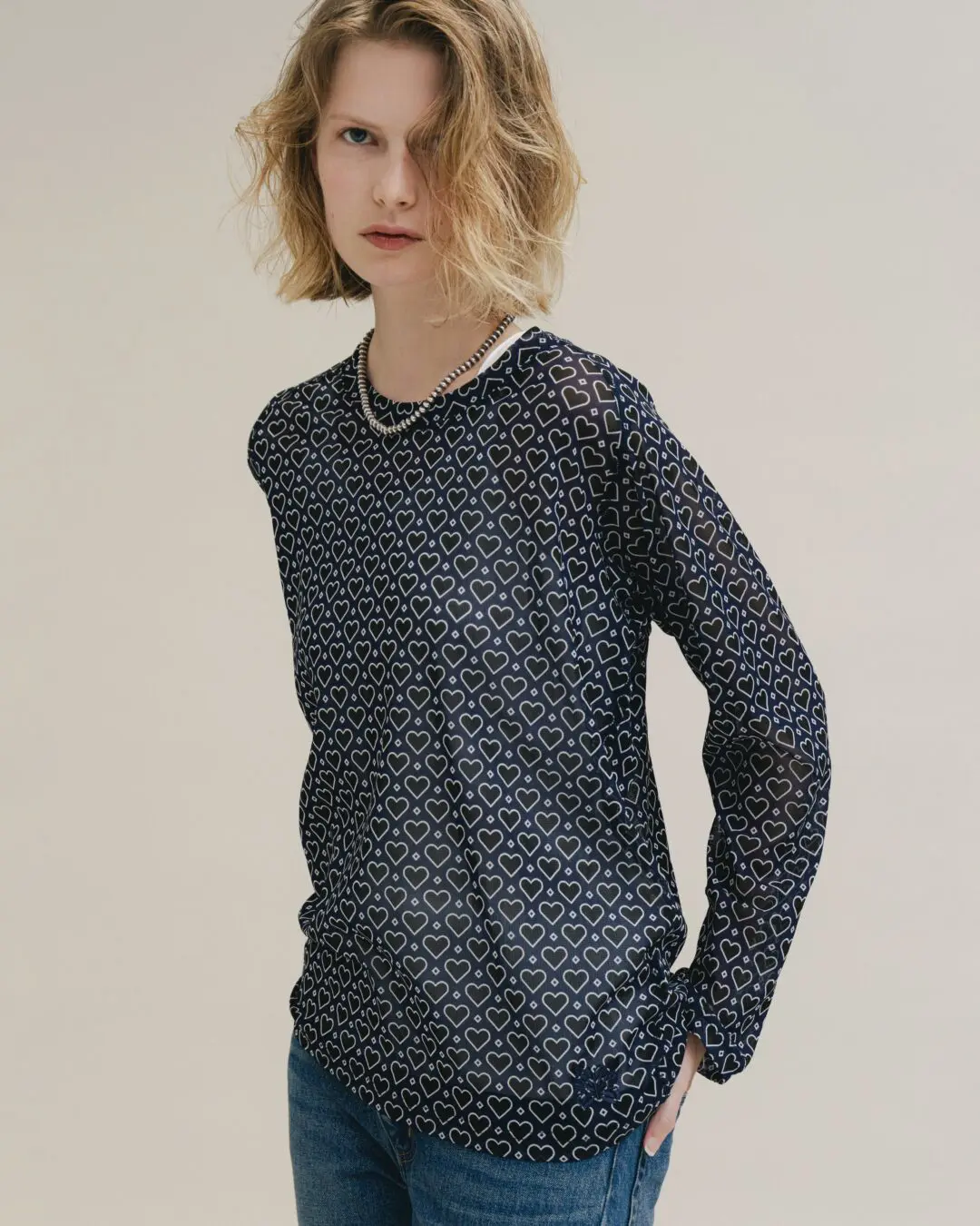 Front-facing studio portrait of a model wearing a navy heart-print Needles x BEAMS BOY long-sleeve shirt paired with denim, showcasing the collabs play pattern