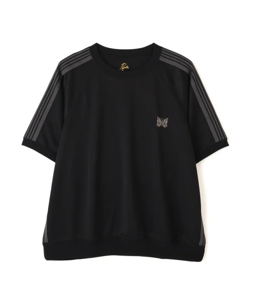 Close-up product image of the NEEDLES “Track S/S Crew Neck Shirt – Poly Smooth” in an understated black colorway with tonal charcoal striping. The oversized short-sleeve silhouette features raglan sleeves, ribbed hems, and the brand’s signature embroidered Papillon butterfly logo at the chest, delivering a refined balance between retro athleticwear and elevated Japanese streetwear minimalism