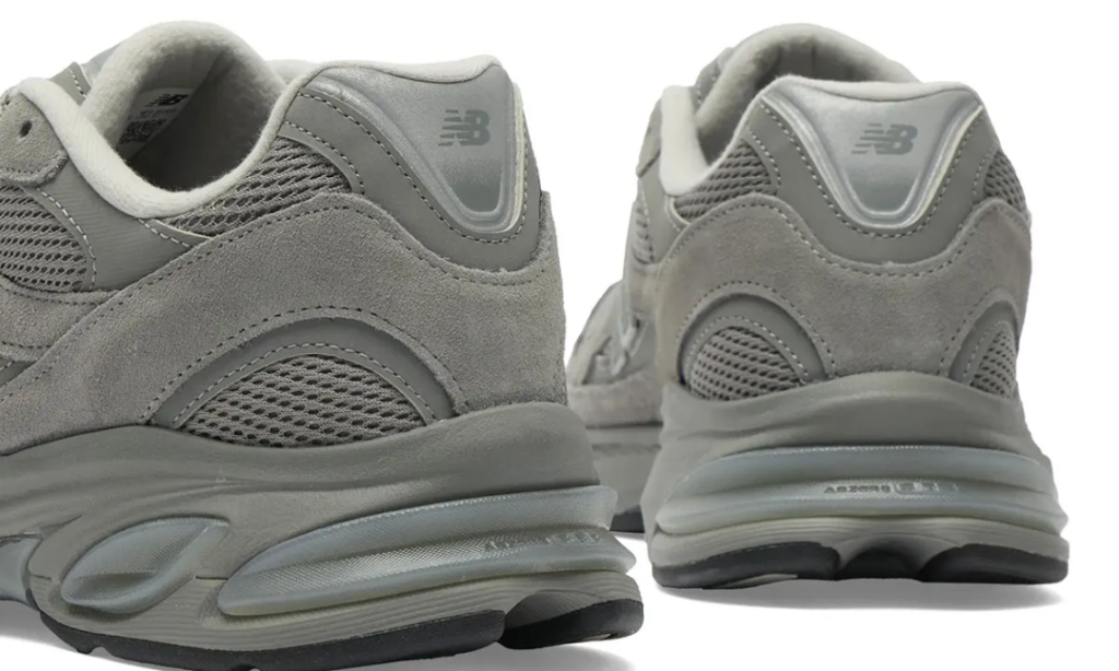 A rear-angle close-up of the New Balance U2010 3EJ “Harbor Grey” highlights the sculpted heel construction and layered material composition that define the silhouette’s modern retro identity. Soft grey suede wraps around breathable mesh underlays and tonal synthetic heel panels, while subtle New Balance branding blends seamlessly into the monochromatic palette. The enlarged ABZORB cushioning pods become especially prominent from this perspective, emphasizing the shoe’s comfort-focused engineering and fluid Y2K-inspired sole geometry that merges performance heritage with understated contemporary style