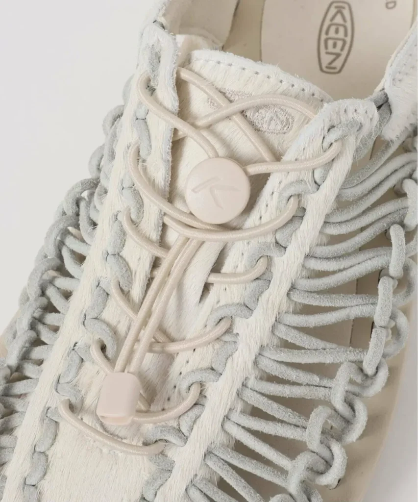 Close-up of the KEEN sandal upper highlighting elastic speed laces with toggle fastening, soft suede-like woven cords, and textured cream leather panels
