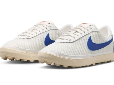 White mesh low-profile Nike shoe with vivid royal blue Swooshes, cream-tinted midsoles, and rugged waffle-inspired outsoles, blending vintage track aesthetics with lightweight modern texture