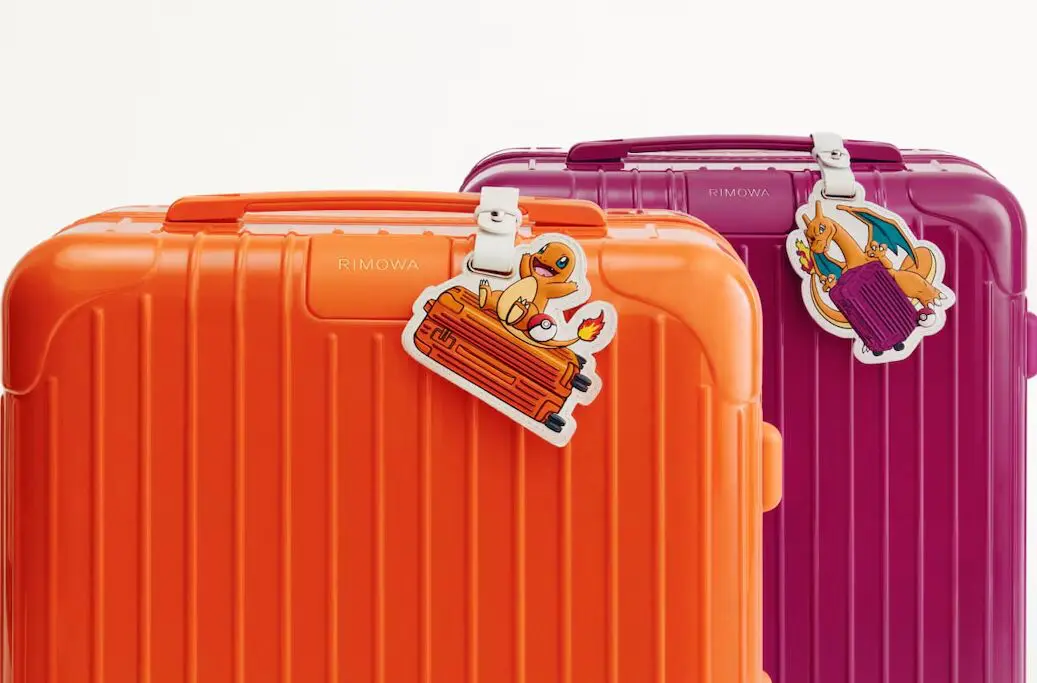 Colorful RIMOWA suitcases in orange and magenta displayed with Pokémon-themed leather luggage charms featuring Charmander and Charizard, celebrating Pokémon’s 30th anniversary collab