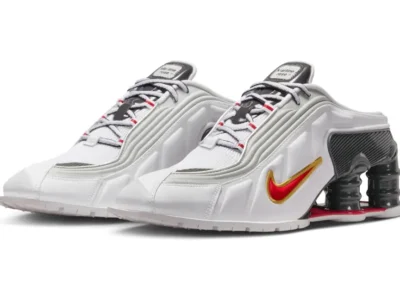 Martine Rose x Nike Shox MR4 Mule in White/Fire Red displayed from a three-quarter angle, featuring a sculpted white upper, metallic detailing, red-and-gold Swoosh branding, and oversized black Shox cushioning columns