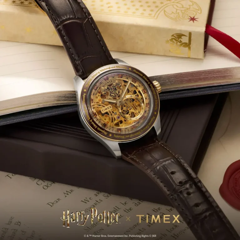 Close-up campaign image of the Timex x Harry Potter and the Philosopher's Stone Waterbury Skeleton Automatic watch featuring a gold-toned exposed mechanical dial, Hogwarts crest detailing, brown crocodile-grain leather strap, and engraved bezel resting atop an open wizard-themed book beside parchment-style packaging