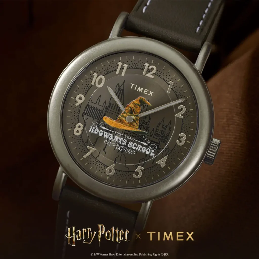 Close-up campaign image of the Timex x Harry Potter and the Philosopher's Stone Hogwarts-themed watch featuring a dark gray dial with illustrated Hogwarts castle artwork, oversized Sorting Hat graphic across the center, vintage-style numeral markers, matte gunmetal case, and black leather strap with contrasting white stitching