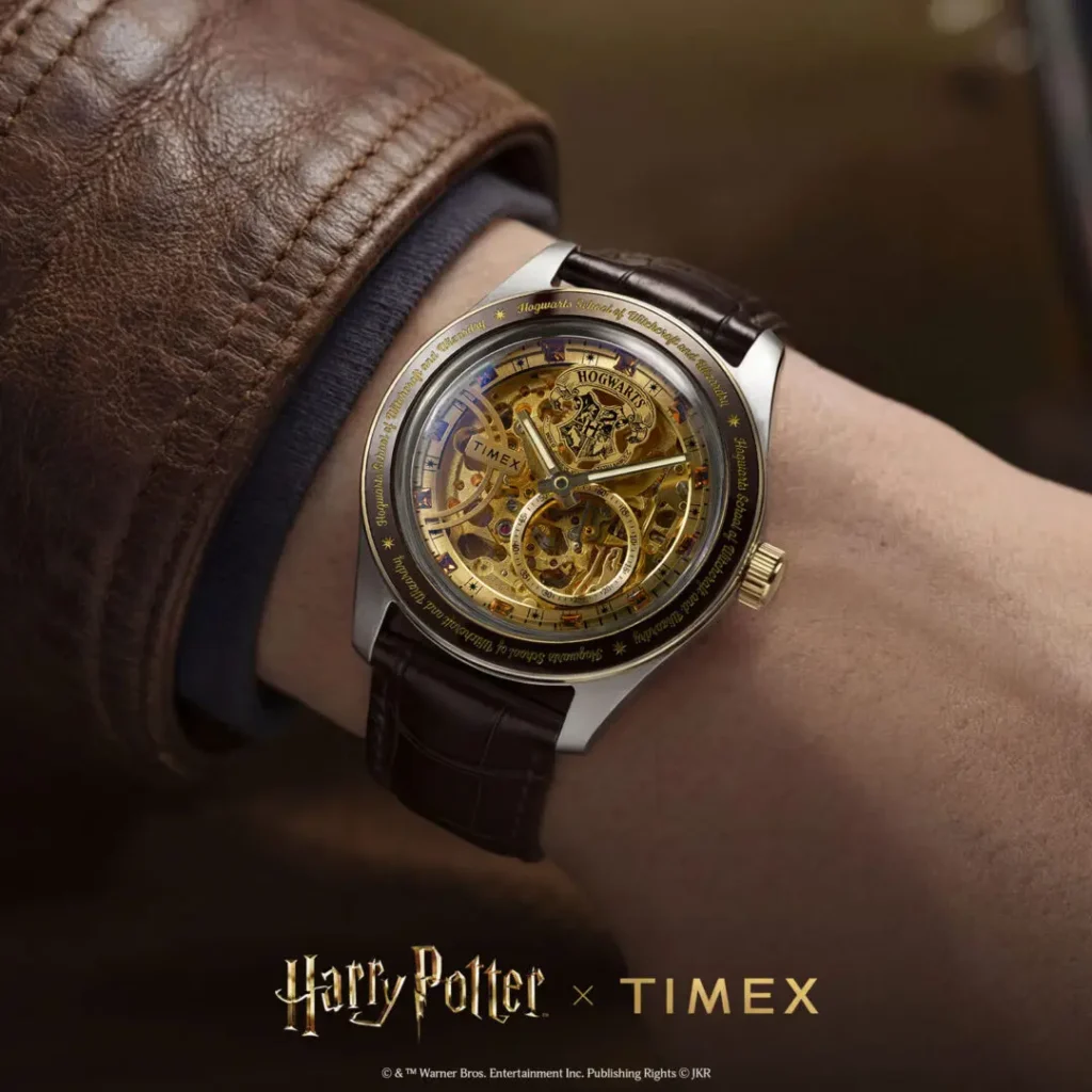 On-wrist campaign shot of the Timex x Harry Potter and the Philosopher's Stone Waterbury Skeleton Automatic featuring a gold-toned open-work dial, Hogwarts crest at 12 o’clock, engraved dark bezel, and brown crocodile-grain leather strap styled beneath a brown leather jacket sleeve