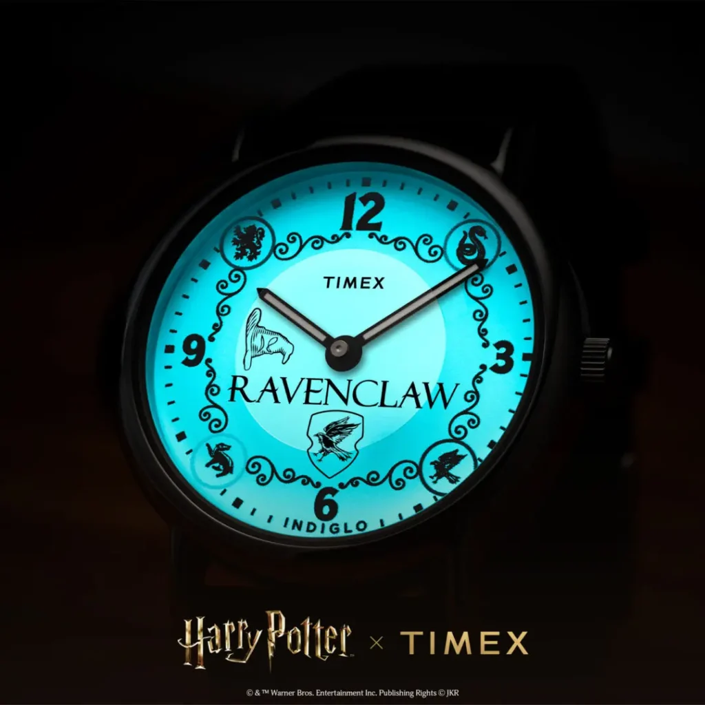 Close-up low-light campaign image of the Timex x Harry Potter and the Philosopher's Stone Ravenclaw Weekender watch illuminated with blue INDIGLO® backlighting, featuring Ravenclaw crest branding, Sorting Hat graphic, ornate black detailing, and bold numeral markers against a dark background