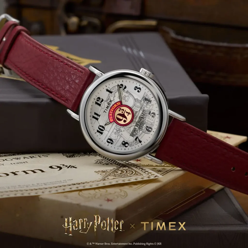 Lifestyle campaign image of the Timex x Harry Potter and the Philosopher's Stone Platform 9¾ watch featuring a silver-toned dial with illustrated Hogwarts Express artwork, oversized Platform 9¾ centerpiece graphic, polished silver-tone case, and burgundy leather strap, styled atop wizard-themed books and Hogwarts travel ephemera