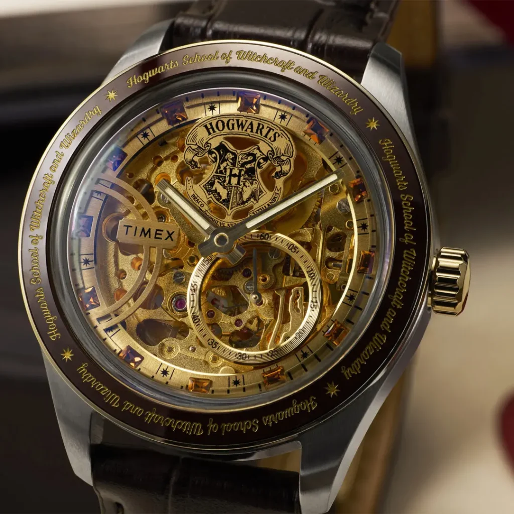 Macro close-up of the Timex x Harry Potter and the Philosopher's Stone Waterbury Skeleton Automatic showcasing the exposed gold-toned mechanical movement, Hogwarts crest detailing, faceted crystal hour markers, engraved “Hogwarts School of Witchcraft and Wizardry” bezel, and polished stainless steel case with brown leather strap