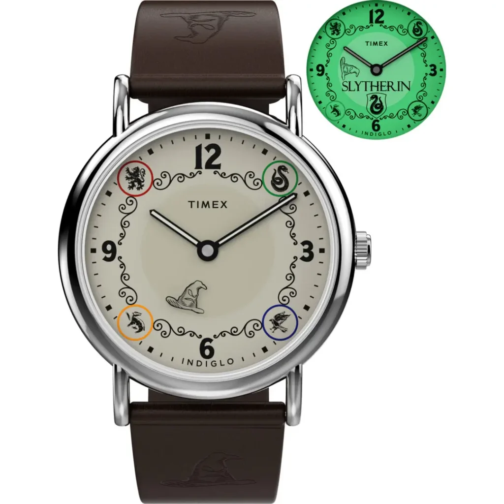 Studio product image of the Timex x Harry Potter and the Philosopher's Stone Slytherin Weekender watch featuring a cream dial with Hogwarts house emblems, Sorting Hat illustration at 6 o’clock, polished silver-tone case, brown leather strap embossed with Sorting Hat graphics, and a green INDIGLO® backlight preview displaying Slytherin branding