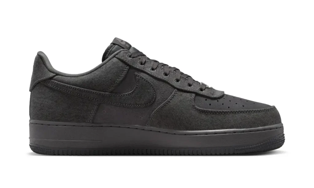 Side profile of the Nike Air Force 1 Low “Denim/Anthracite/Medium Ash,” featuring a monochromatic anthracite finish with textured denim paneling, tonal suede overlays, a darkened Nike Swoosh, perforated toe detailing, matching laces, and an all-black Air sole against a clean light grey studio backdrop