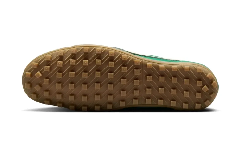 Bottom outsole view of the green Nike Cortez-style turf shoe, showcasing a translucent gum rubber sole with evenly spaced square traction studs and diagonal groove detailing. The retro-inspired tread pattern emphasizes indoor and artificial turf performance while complementing the sneaker’s vintage football aesthetic.