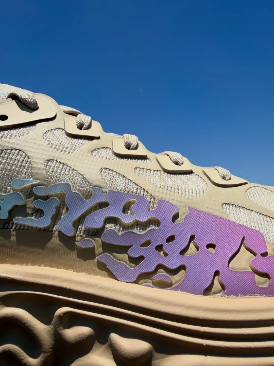 Close-up of a cream-toned sneaker heel featuring cutout branding and raised “Salehe Bembury” lettering, photographed outdoors under direct sunlight against a clear blue sky, emphasizing layered textures and shadow play across the upper