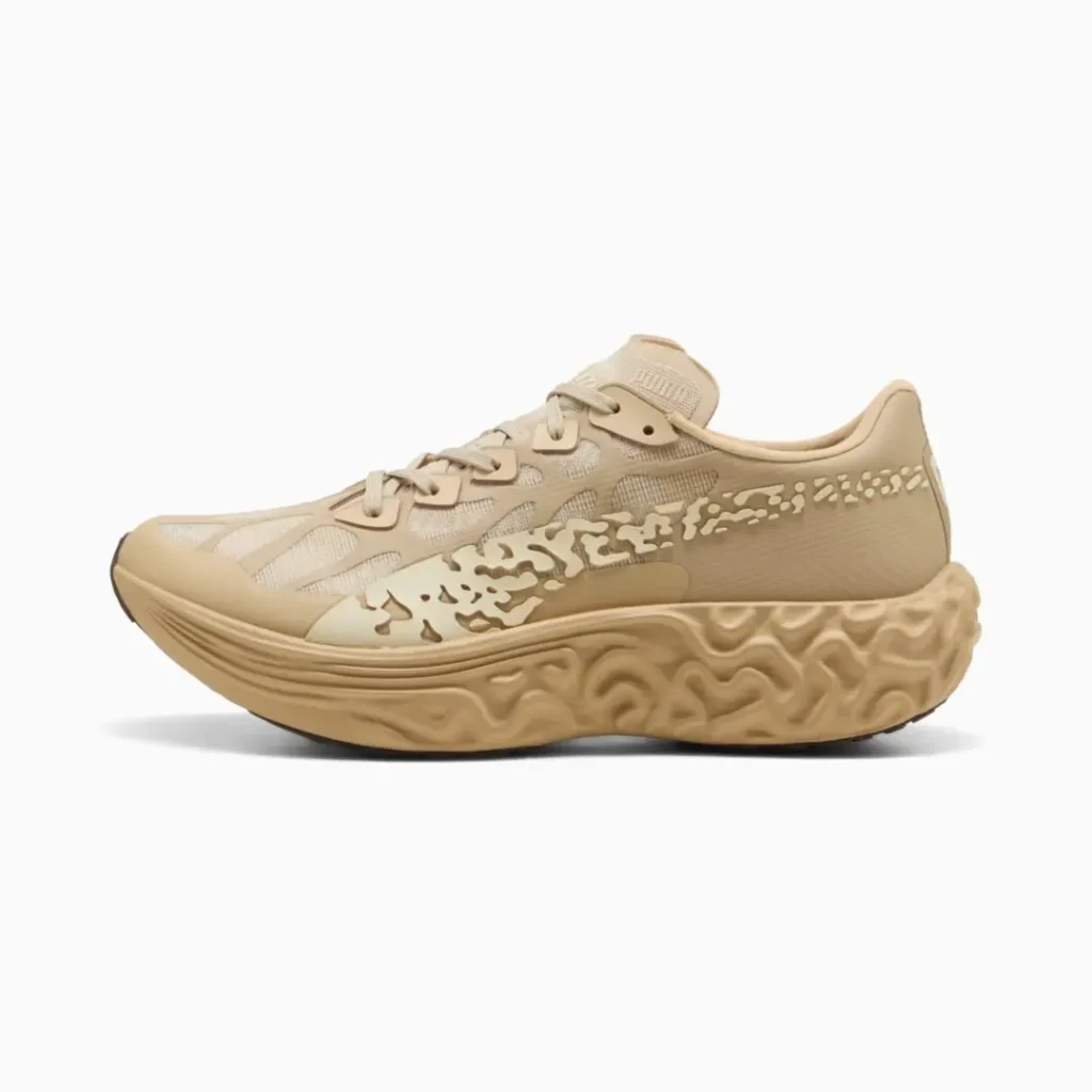 Side profile of a monochromatic beige shoe showcasing technical mesh panels, abstract organic overlays, and a sculptural cushioned midsole with terrain-inspired texture