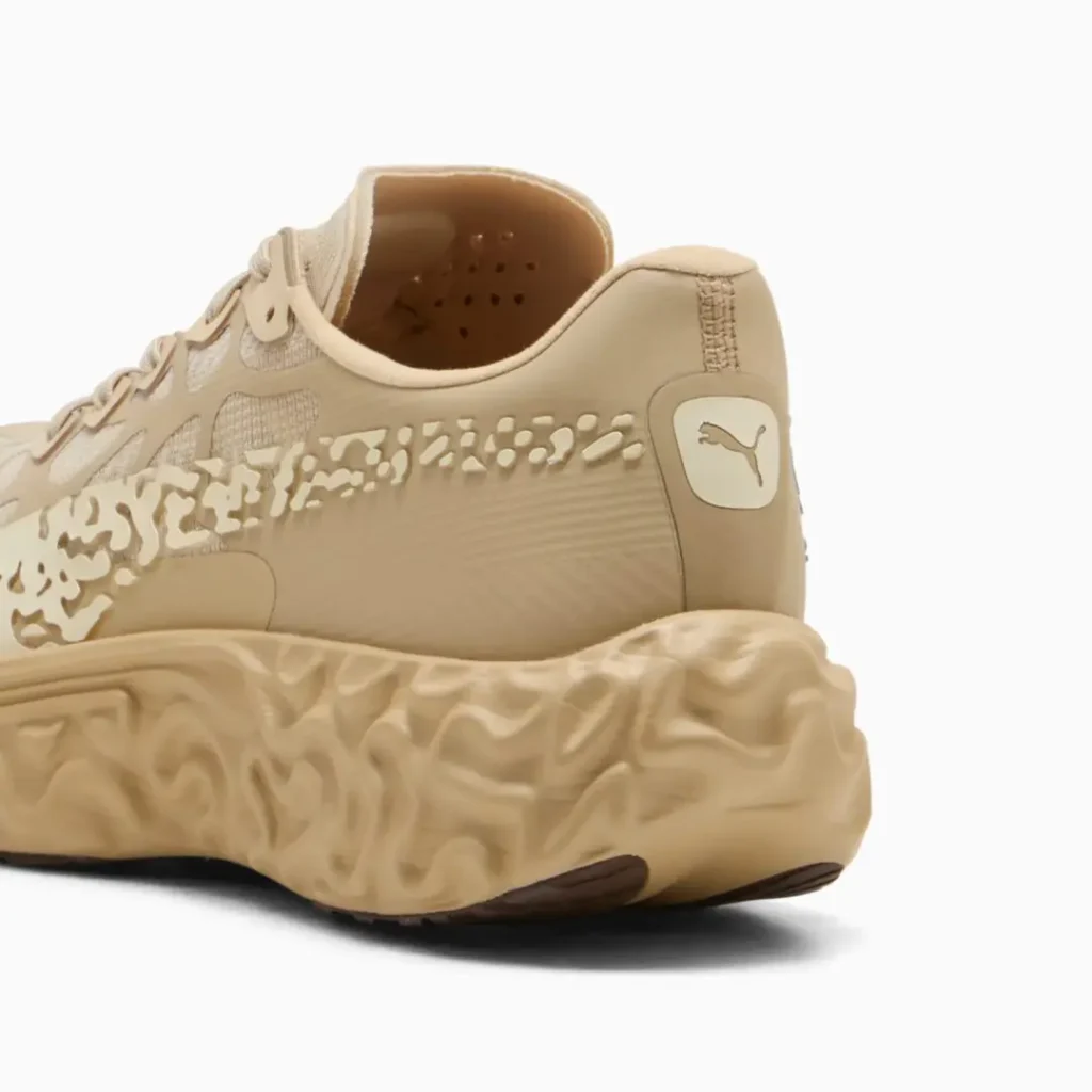 Rear-side close-up of the sneaker showing molded heel construction, tonal logo detail, flowing side graphics, and an embossed textured midsole with sculptural contour