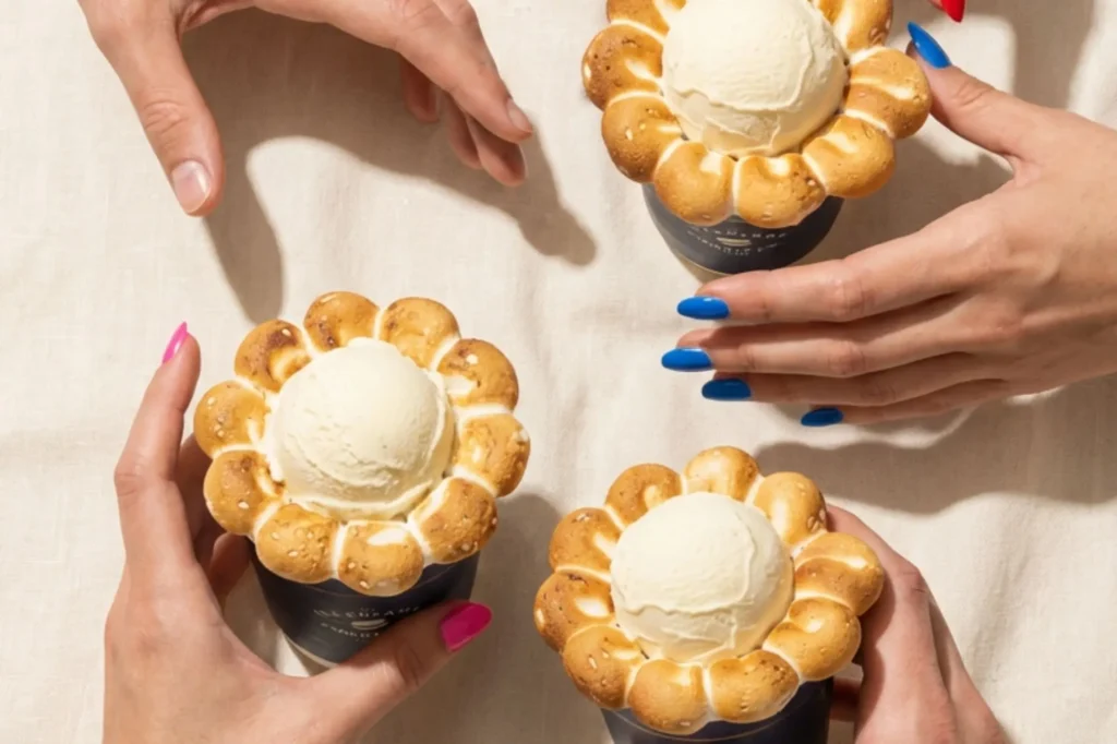 Overhead view of three ICC Cloud Cotton Candy desserts topped with scoops of vanilla ice cream and surrounded by torched marshmallow rings, as multiple hands with colorful manicures reach in to share the experience