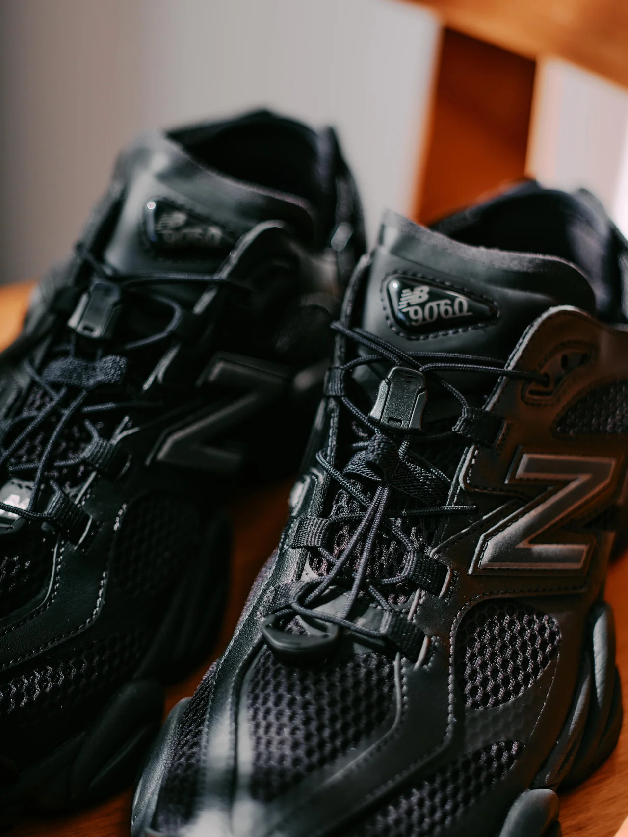 Close-up of black New Balance U9060 hybrid shoe-sandal showing mesh ventilation panels, oversized tonal N logo, toggle quick-lace system, and glossy layered overlays under warm indoor lighting