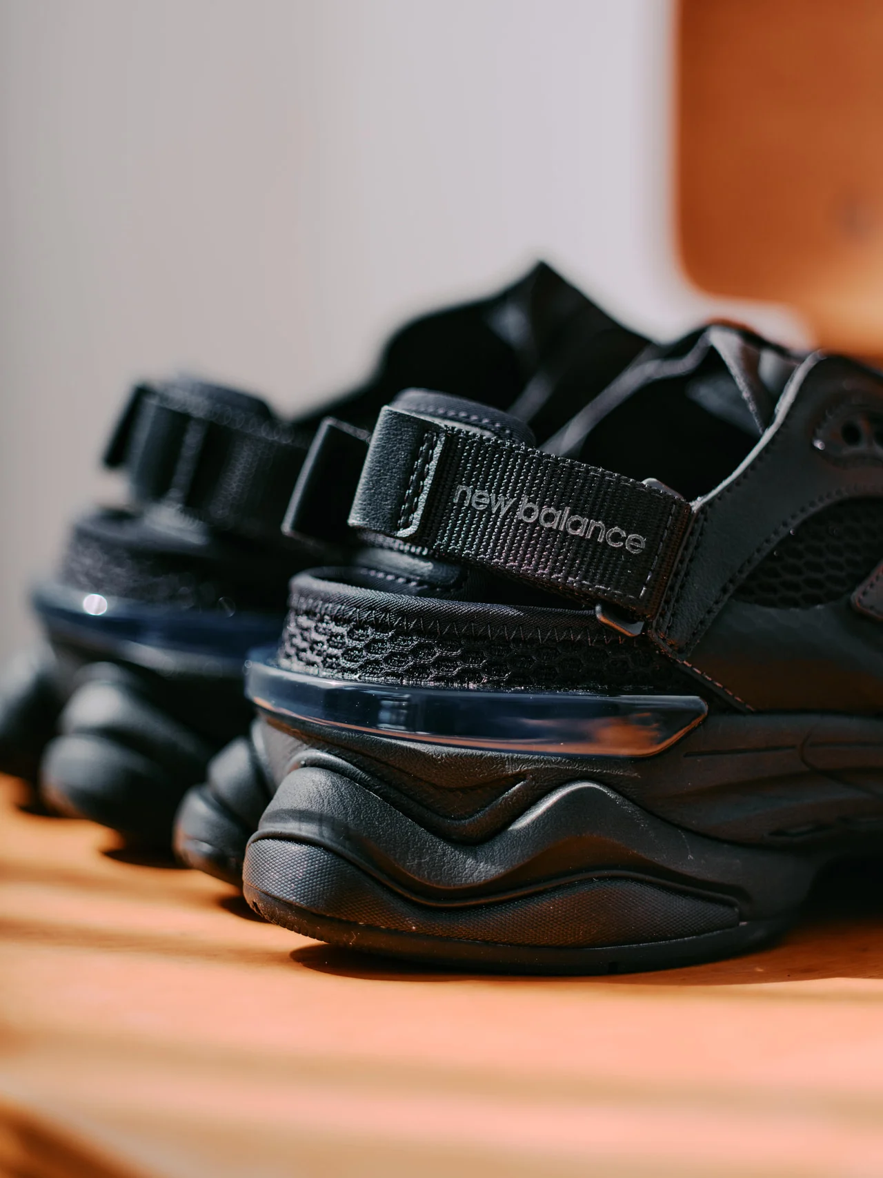 Close-up of black New Balance U9060 hybrid shoe-sandal showing mesh ventilation panels, oversized tonal N logo, toggle quick-lace system, and glossy layered overlays under warm indoor lighting