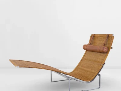 Side profile of the Poul Kjærholm PK 24 hammock lounge chair featuring woven cane seating, cylindrical leather headrest, and polished stainless steel frame