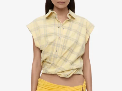 Model wearing a sleeveless pale yellow plaid Christopher Esber shirt styled with an asymmetrical draped yellow mini skirt featuring gathered detailing and a sculptural side cut-out against a clean studio backdrop