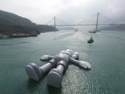KAWS HOLIDAY giant floating Companion sculpture reclining in Hong Kong’s Victoria Harbour surrounded by the city skyline