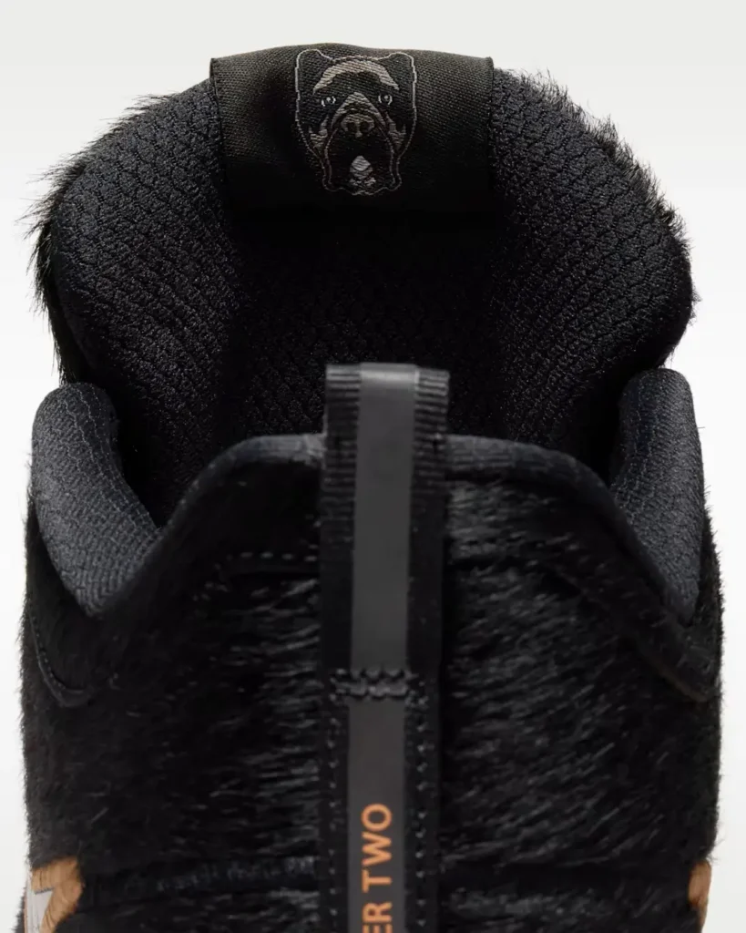 Rear collar view of the black textured sneaker highlighting the embroidered dog graphic on the tongue tab, padded interior lining, and branded heel pull tab