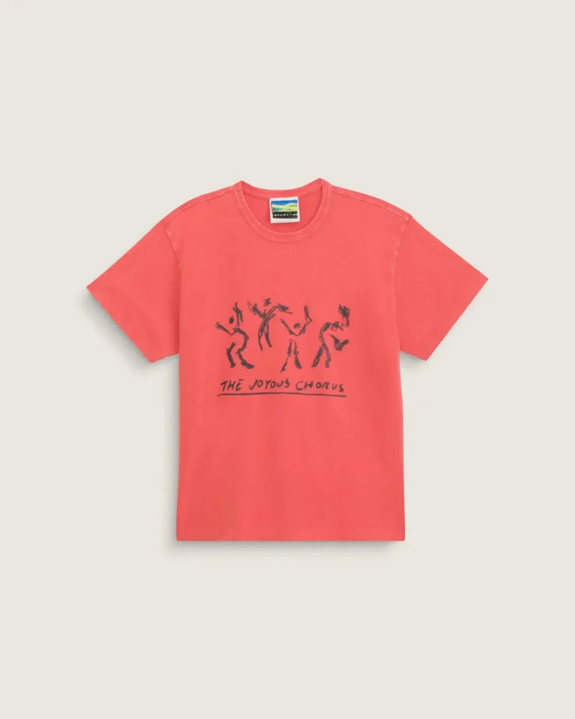 Vintage-washed coral pink graphic T-shirt featuring hand-drawn abstract dancing figures and “The Joyous Chorus” text across the chest, finished with a relaxed fit and minimalist presentation against a soft neutral backdrop