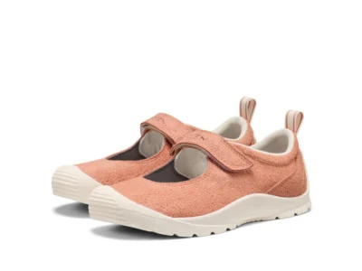 The KEEN Women’s Jasper KM Lite Mary Jane appears in a soft blush-pink colorway with a textured suede-like upper, adjustable hook-and-loop strap closure, rounded toe shape, and off-white cushioned sole. The lightweight silhouette merges outdoor utility with ballet-inspired minimalism, while subtle pull tabs and rugged tread detailing reinforce the model’s hybrid lifestyle functionality