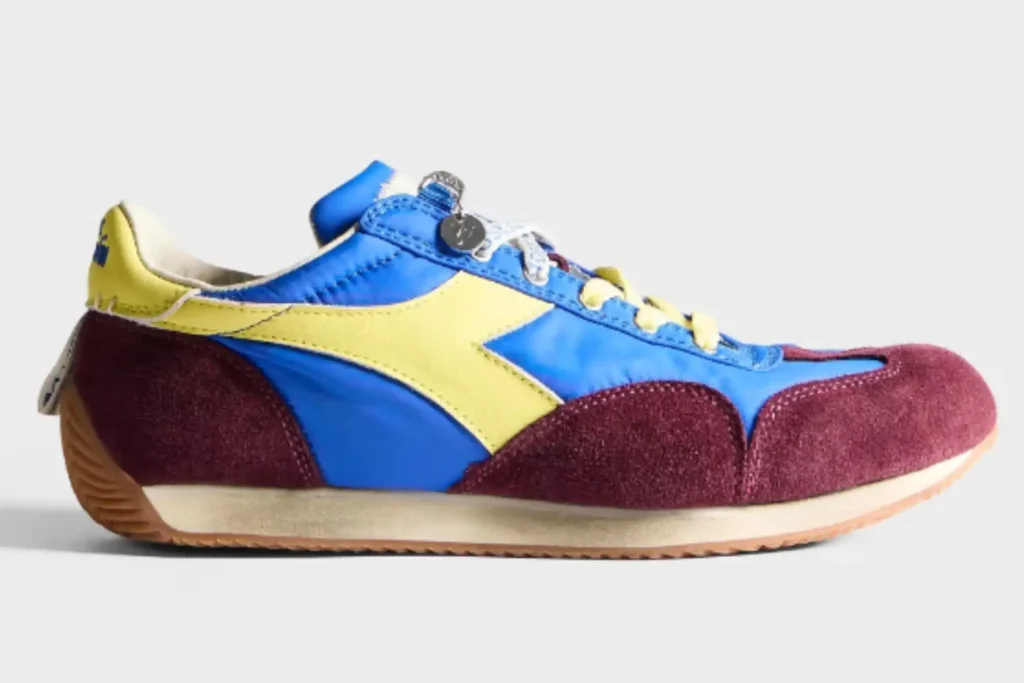 This JW Anderson x Diadora Equipe colorway embraces bold retro contrast through electric blue nylon uppers, rich burgundy suede overlays, and vibrant yellow leather stripes and laces. The saturated palette gives the vintage 1975 runner a more playful, fashion-driven identity while preserving its slim athletic proportions and heritage track-shoe construction. Premium textures and aged sole finishes keep the silhouette grounded in Diadora’s archival roots despite its energetic contemporary style